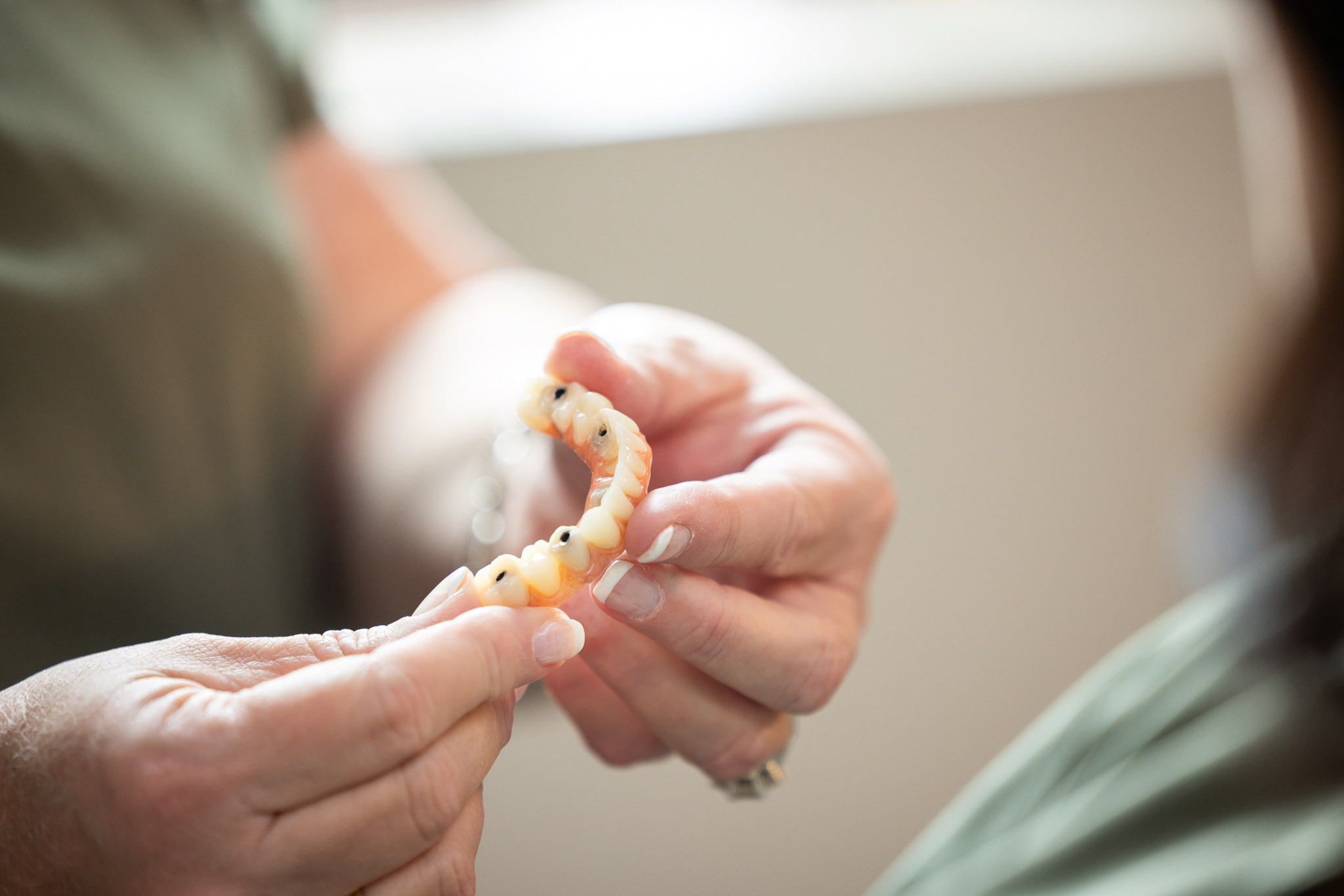 Gloved hands carefully inspecting a multi-tooth dental bridge at Ireland Restorative Dentistry