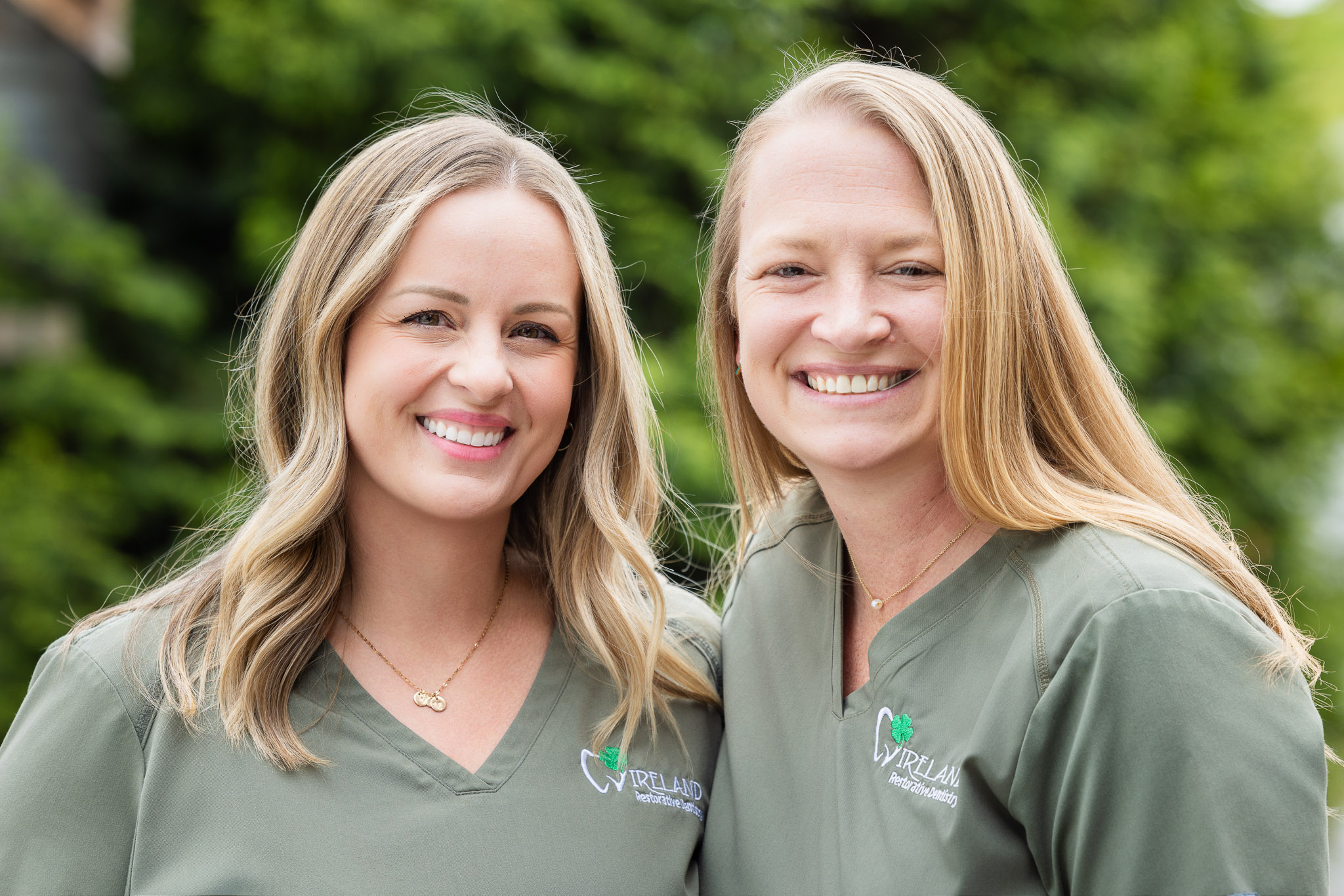 Two Ireland Restorative Dentistry team members in green scrubs laughing together outdoors